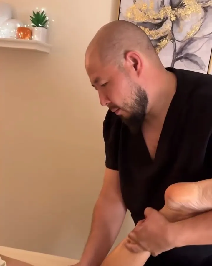 Tony, focused and calm, working on a client's foot, with a framed painting and a shelf behind him